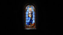 In het aardedonker van de kerk komt het glas-in-loodraam mooi uit.